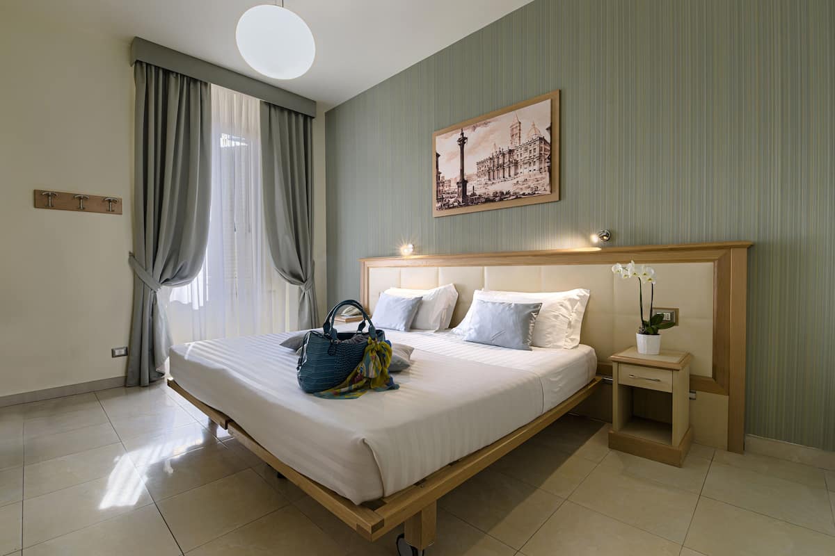 A neatly made bed with white linens, a bedside table with a lamp, and a framed picture on the wall.