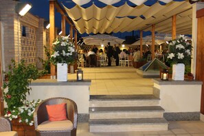 An outdoor dining area with steps leading up to a covered seating area, surrounded by potted plants and outdoor lighting. - Domus Australia (Rome)