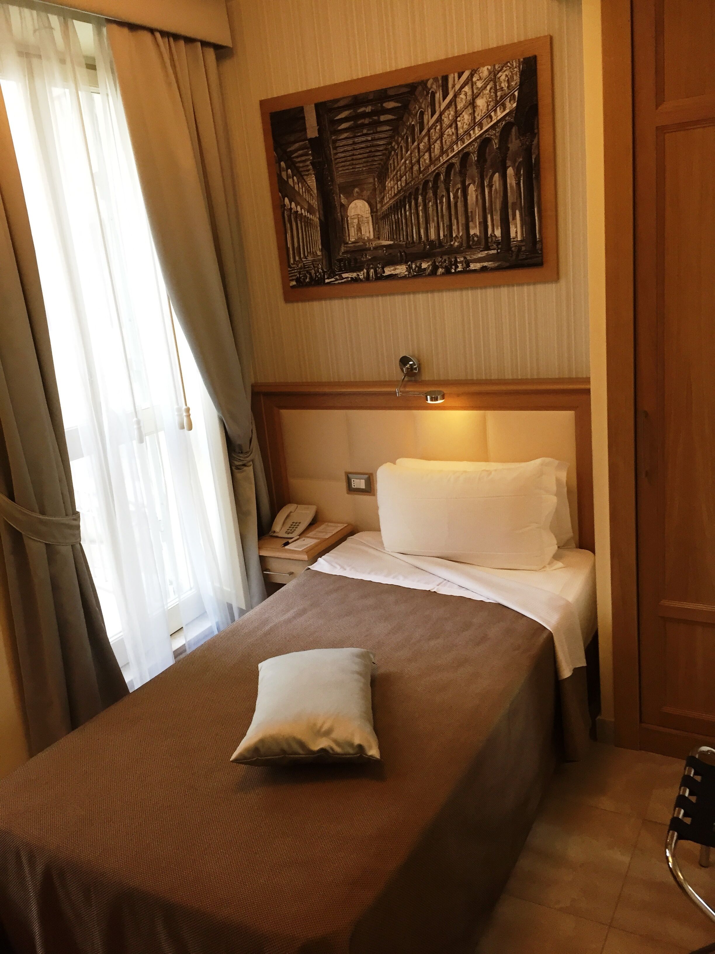 A hotel room with a bed, a bedside telephone, and a painting on the wall.