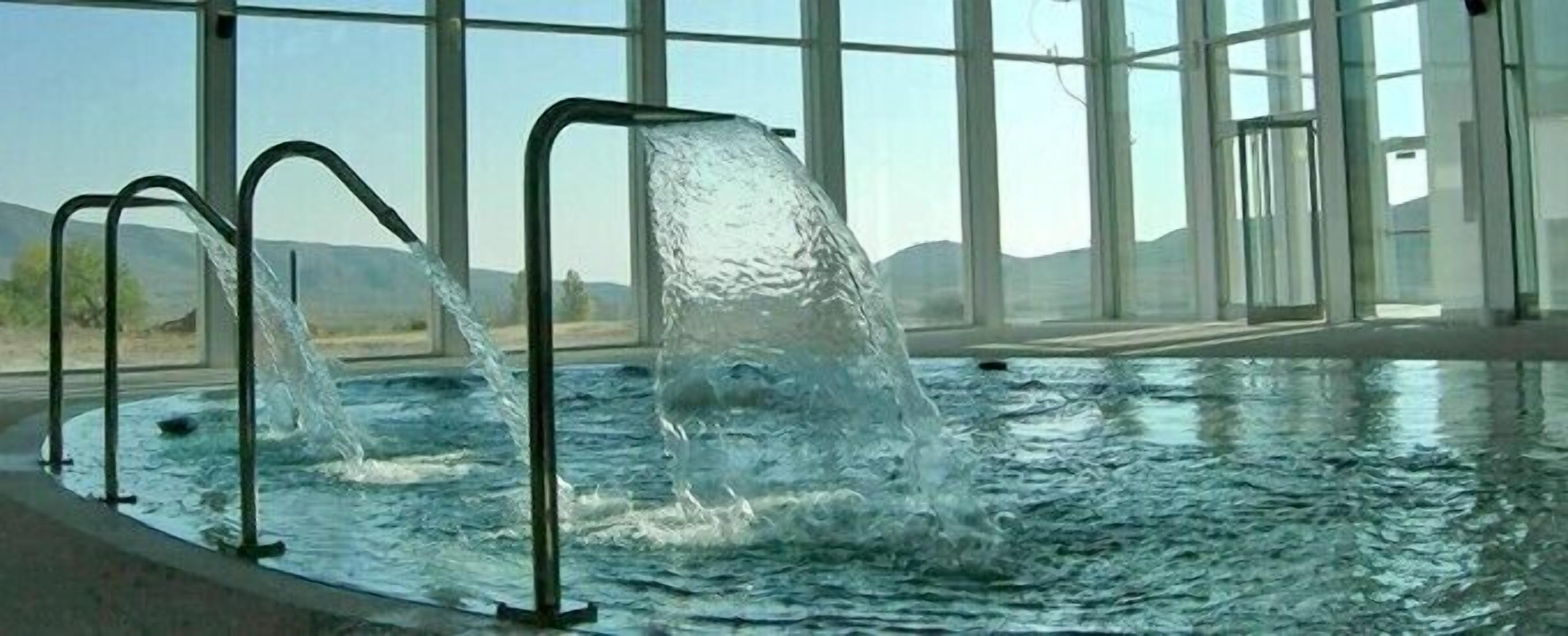 Una piscina con dos chorros de agua y una vista despejada del exterior.