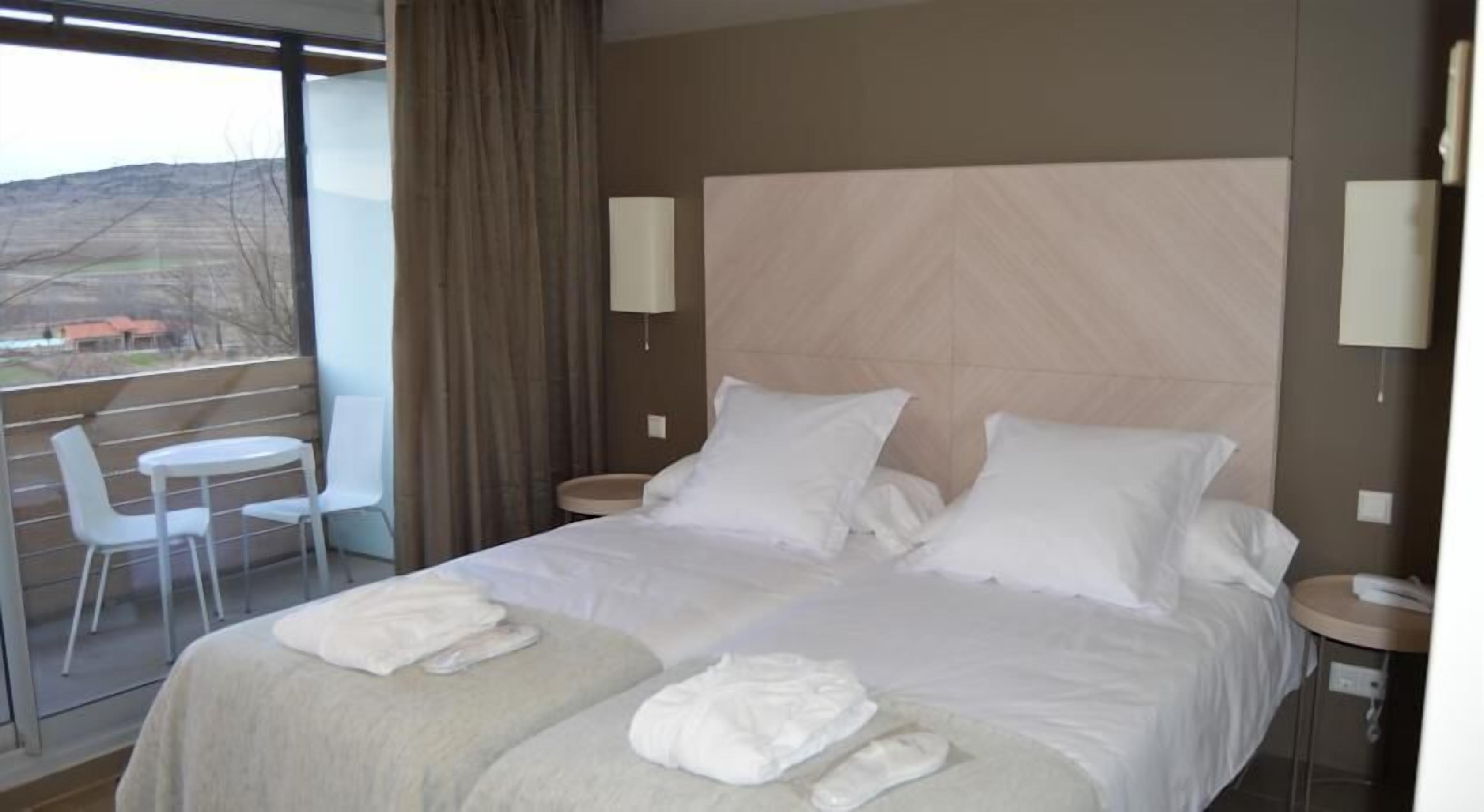 A hotel room with a large bed, two bedside tables, a desk with a chair, and a view of the outdoors.