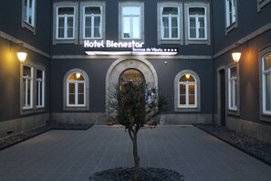 Hotel Bienestar with a central arched entrance, multiple windows, and a small tree in the courtyard.