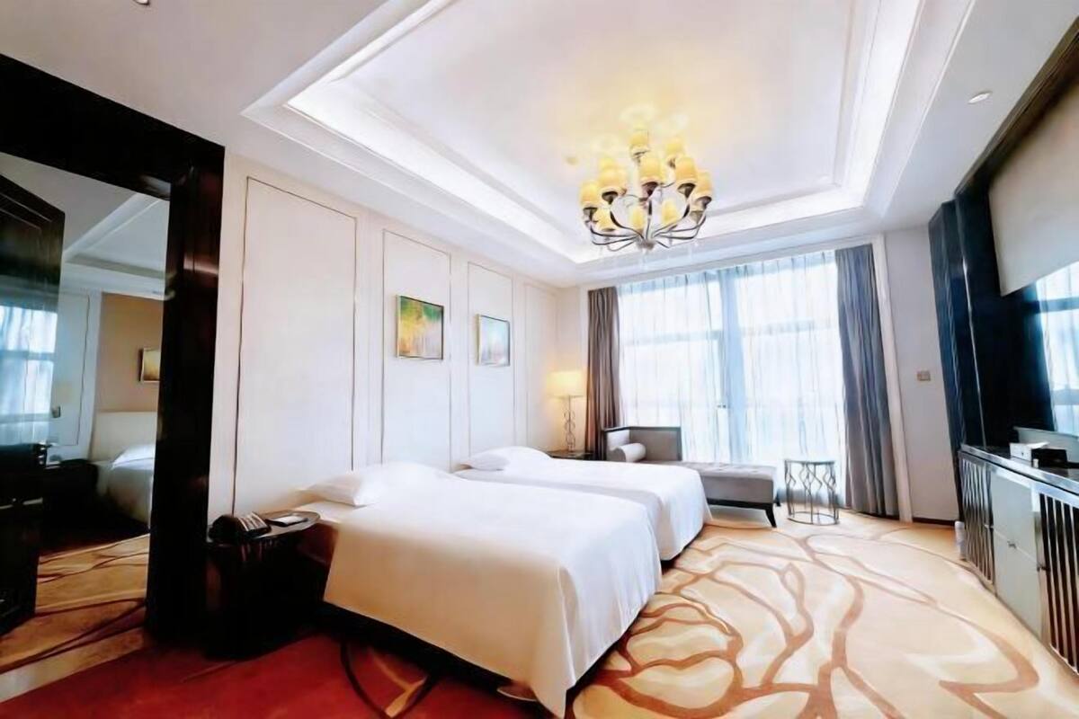 Quarto de hotel com duas camas, um espelho grande, um candelabro e vista para o exterior.