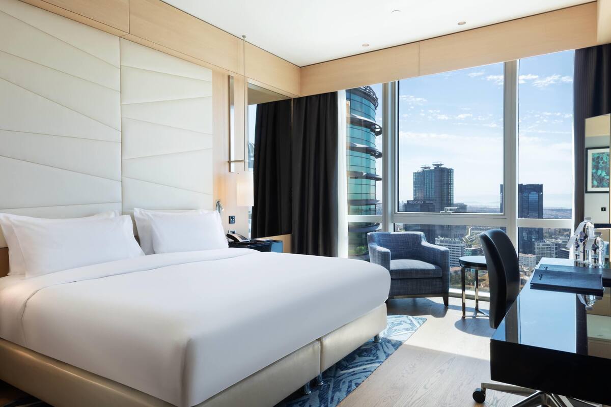 Ein modernes Hotelzimmer mit einem großen Bett, einem Schreibtisch und Blick auf die Stadt.