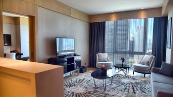 Una habitación de hotel moderna con un ventanal grande, un televisor de pantalla plana, dos sillones, un sofá y una mesa de centro.