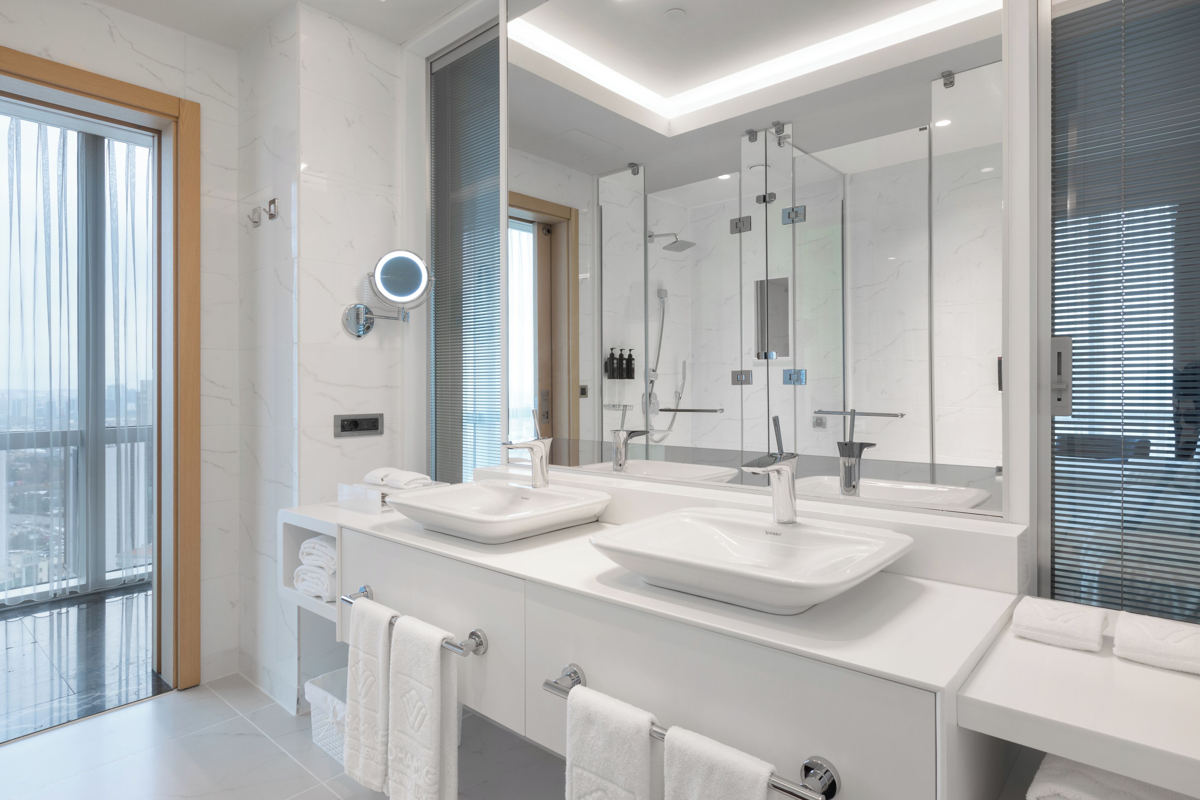 A modern bathroom with two sinks, a large mirror, and a glass shower enclosure.
