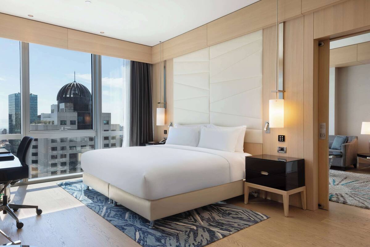 Ein modernes Hotelzimmer mit einem großen Bett, einem Schreibtisch und Blick auf eine Stadtlandschaft.