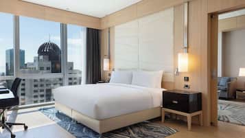 A modern hotel room with a large bed, a desk, and a view of a cityscape.