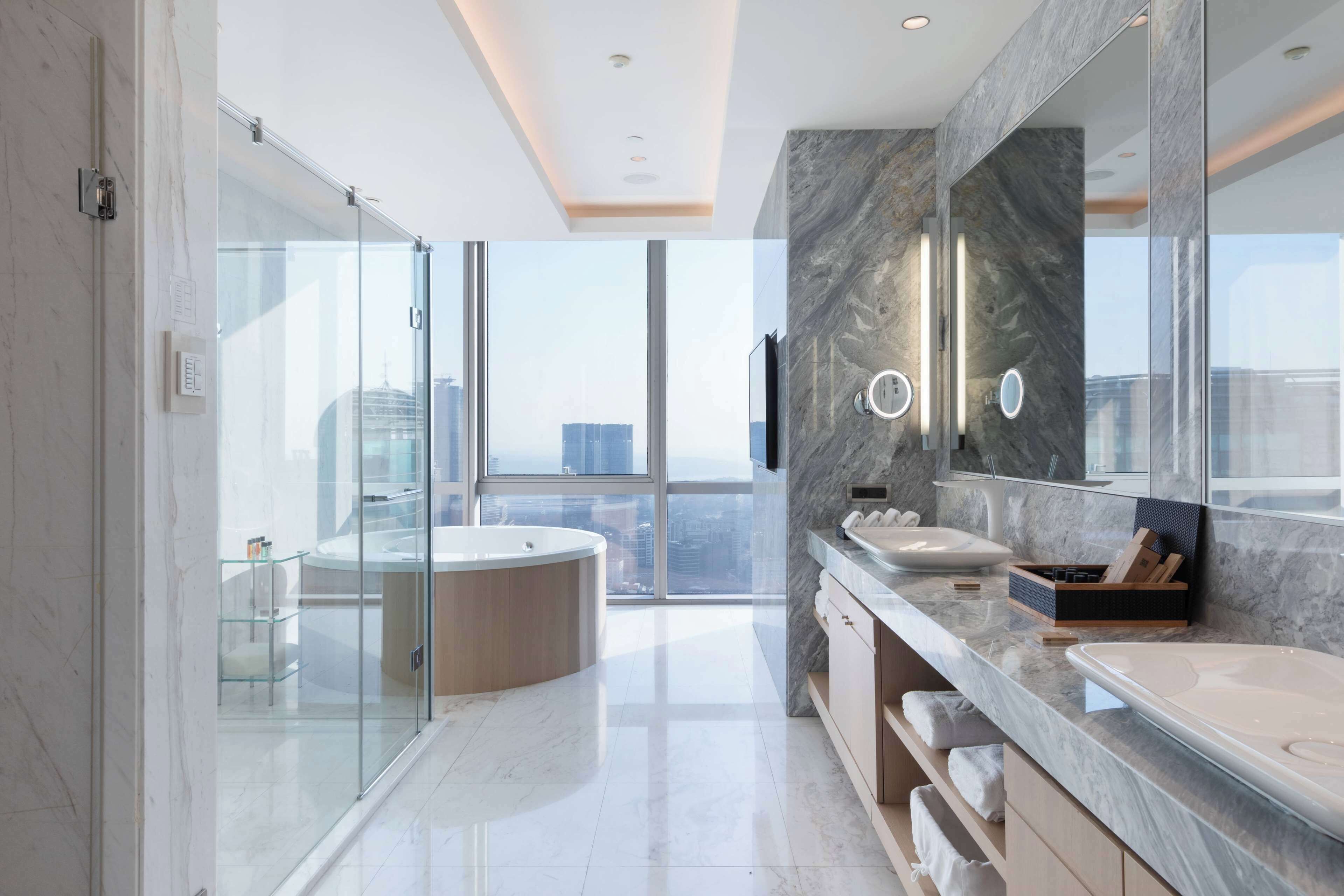 Une salle de bain moderne dotée d’une douche à parois de verre, d’une baignoire sur pieds et d’un grand meuble-lavabo avec un pare-éclaboussures en marbre.