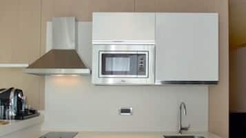 Una cocina compacta con microondas, lavamanos y refrigerador para bebidas.