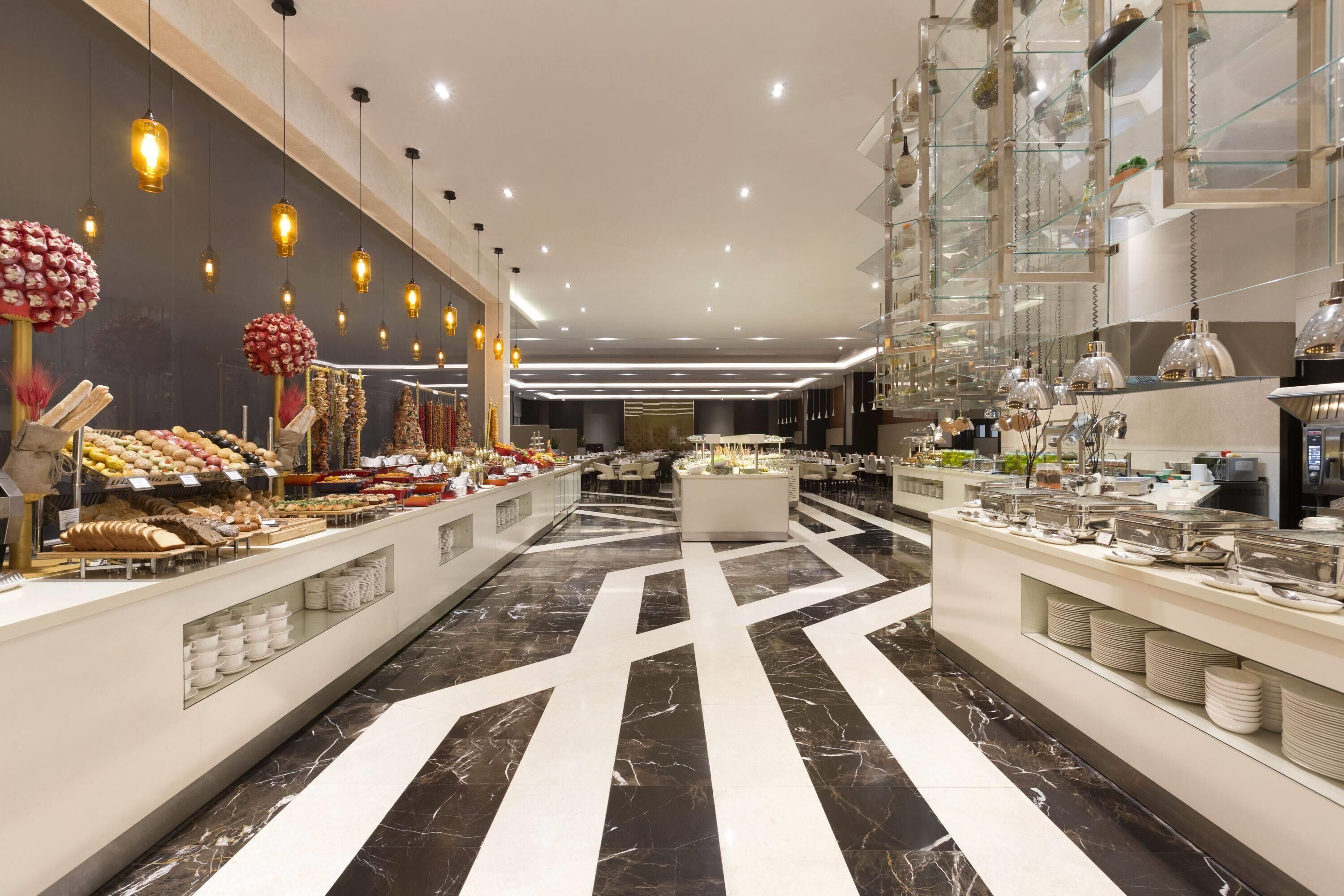 A modern hotel lobby with a marble floor, buffet area, and hanging pendant lights.