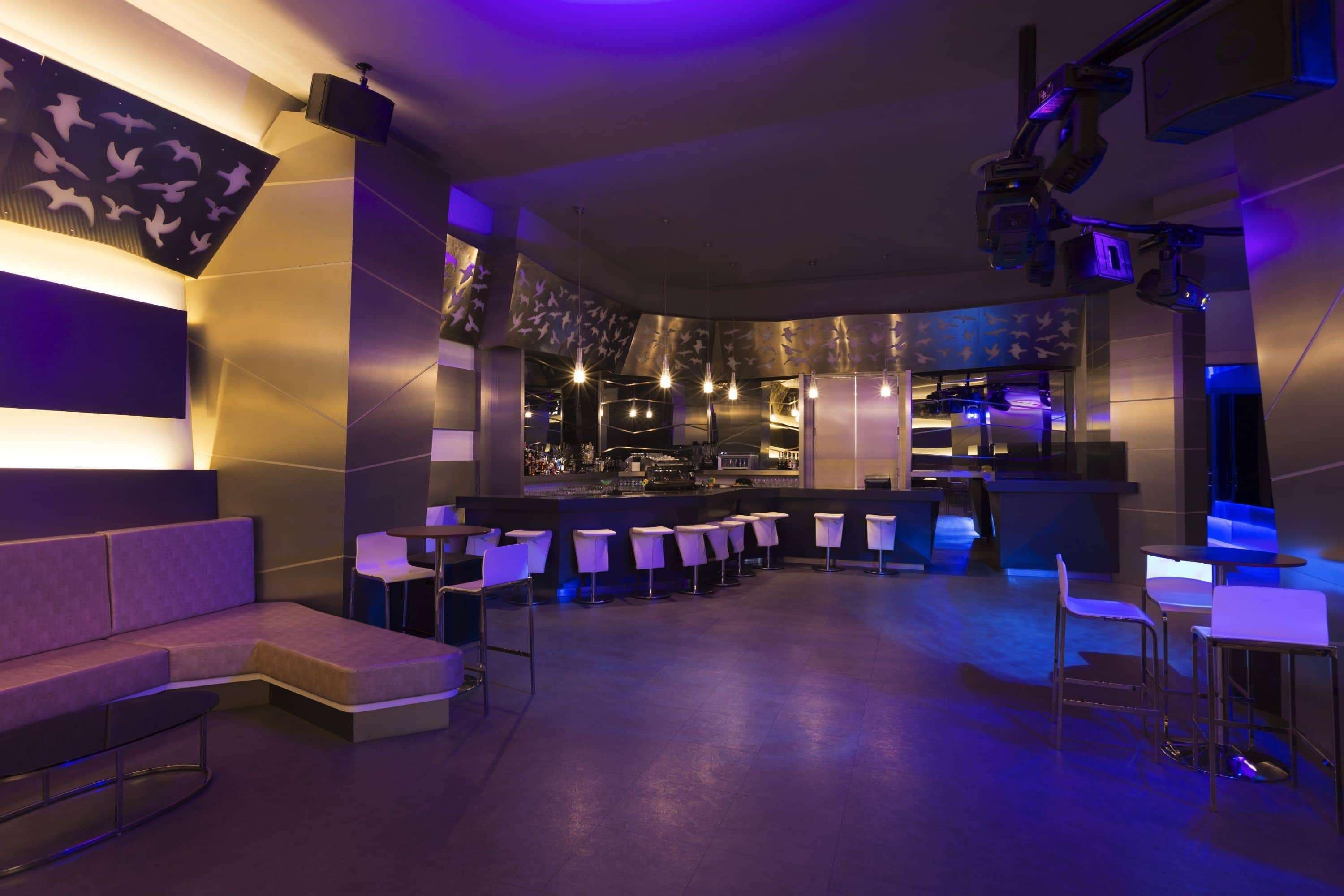 Un área de bar moderna con una disposición de asientos curvada, una barra y vistas de la ciudad a través del ventanal.