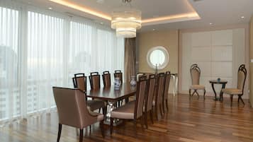 A spacious dining area with a large wooden table, multiple chairs, a chandelier, and large windows with sheer curtains.