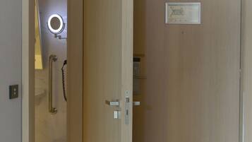 Ein Hotelzimmer-Eingang mit Holztür, Handlauf, Spiegel und einem gerahmten Bild an der Wand.