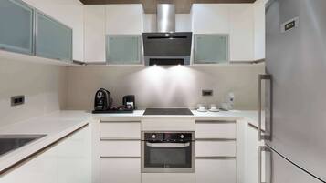 Una cocina moderna con armarios blancos, horno integrado, refrigerador de acero inoxidable y cafetera sobre la encimera.