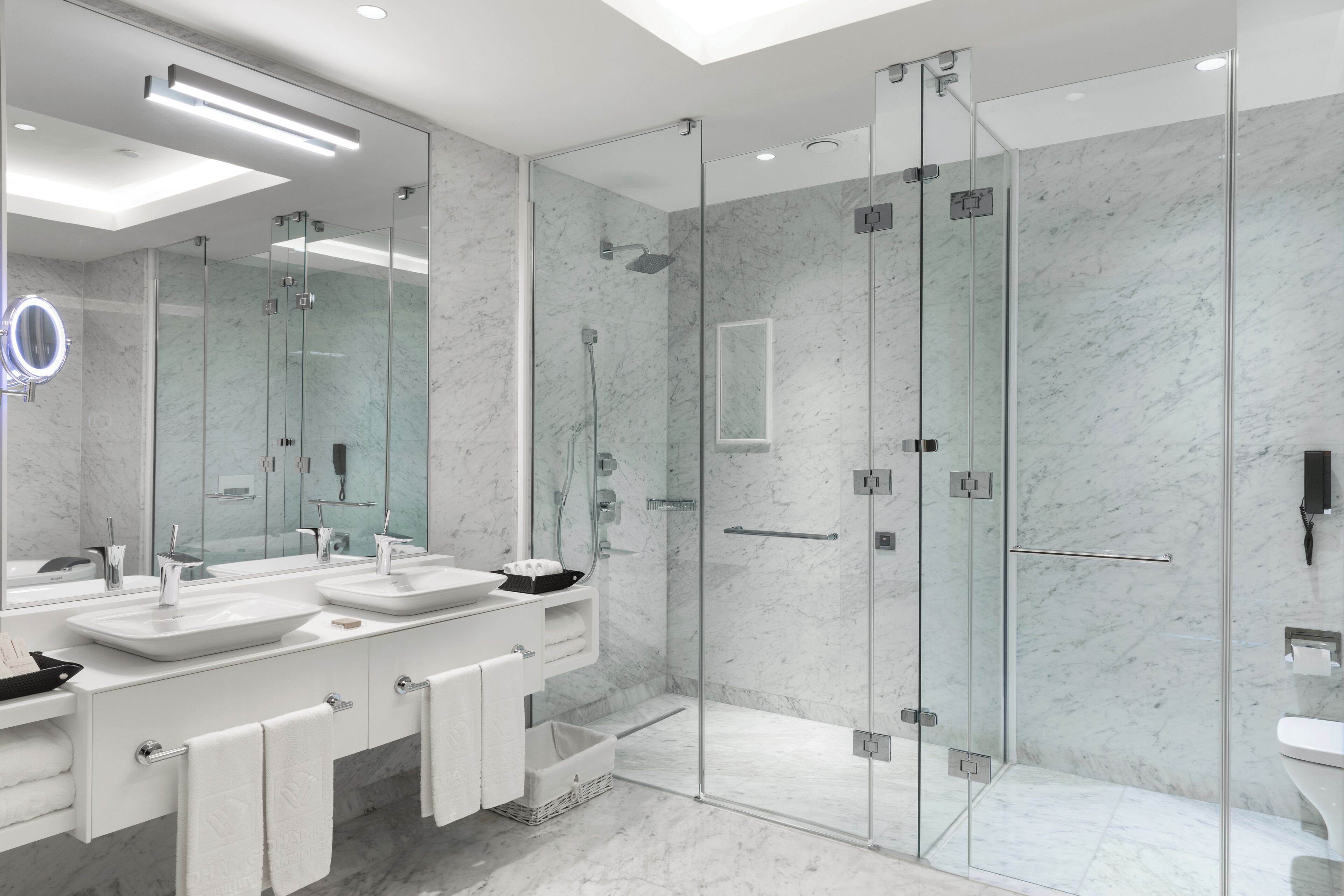 Un baño moderno con dos lavamanos, una ducha con mampara de vidrio y un espejo grande.
