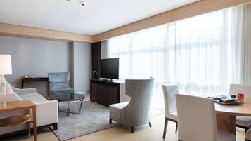 Una habitación de hotel moderna con sofá, sillones, una mesa de comedor, televisor y ventanas amplias.