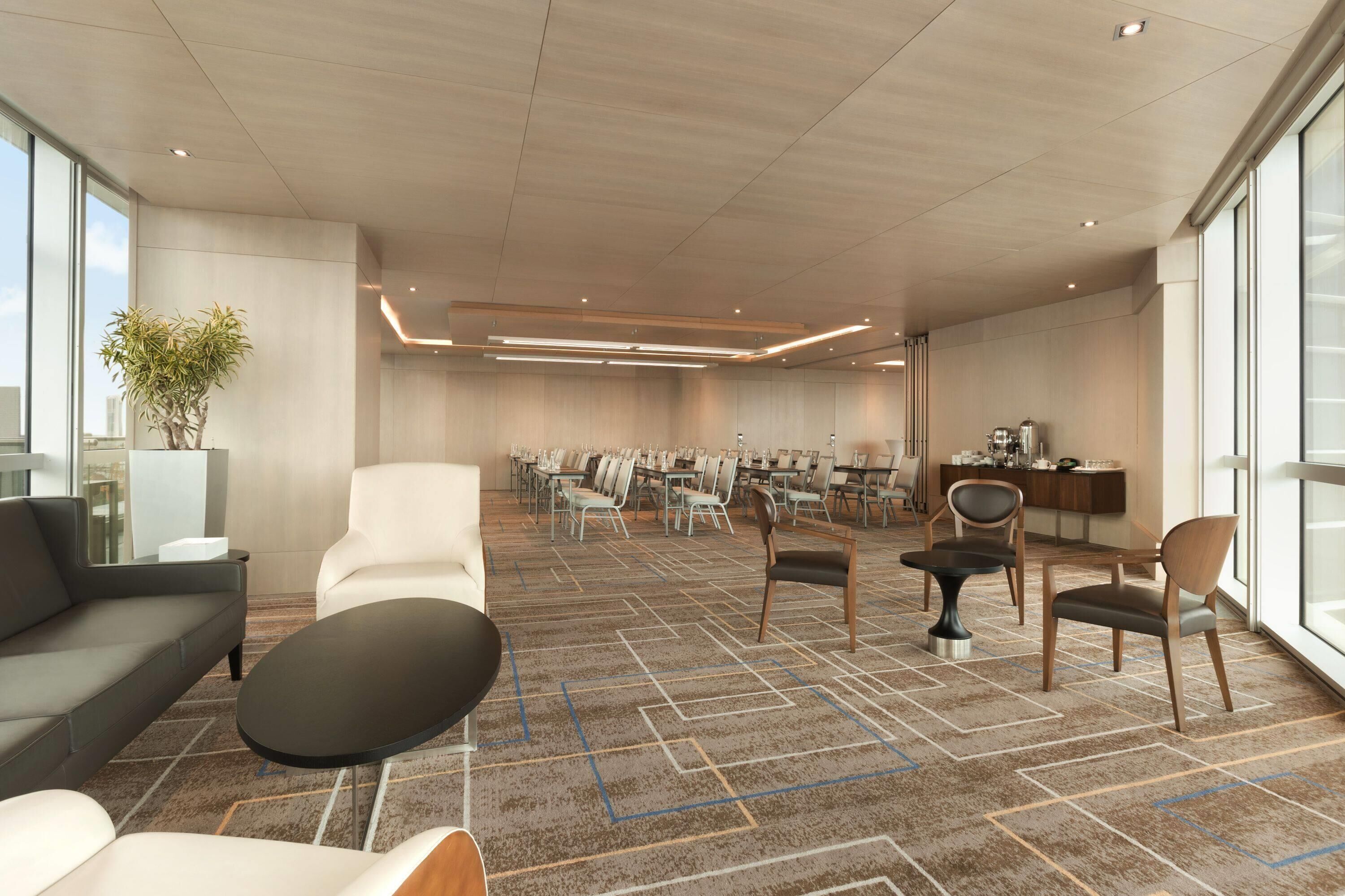 A modern hotel lobby with a seating area, a reception desk, and a large window providing a view of the sky.