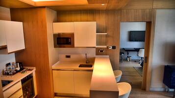 Cocina compacta con electrodomésticos modernos, microondas integrado y pileta. Hay un pequeño espacio de descanso con una silla y una mesa.