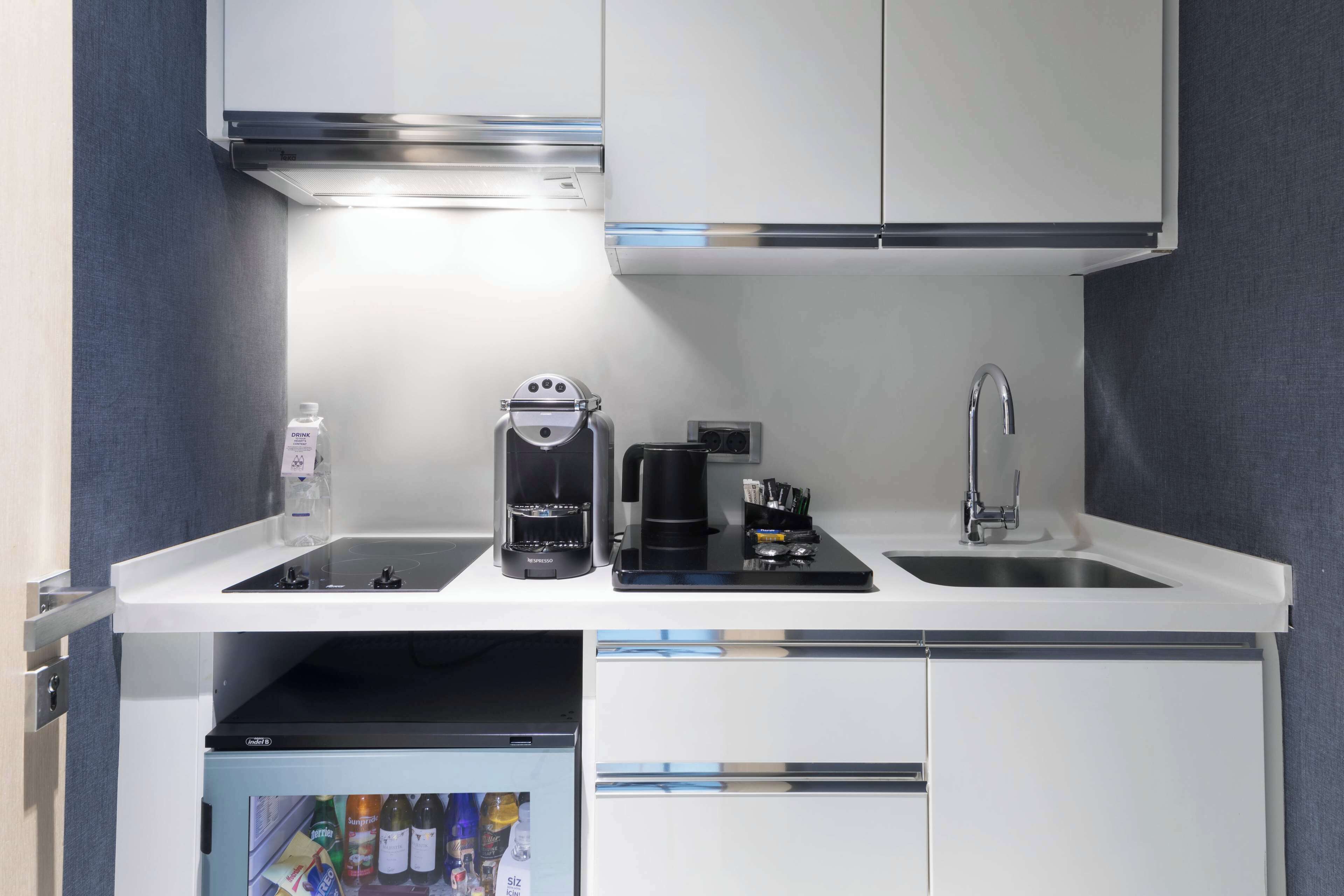 Una cocina compacta con cafetera integrada, un lavamanos y un refrigerador pequeño.