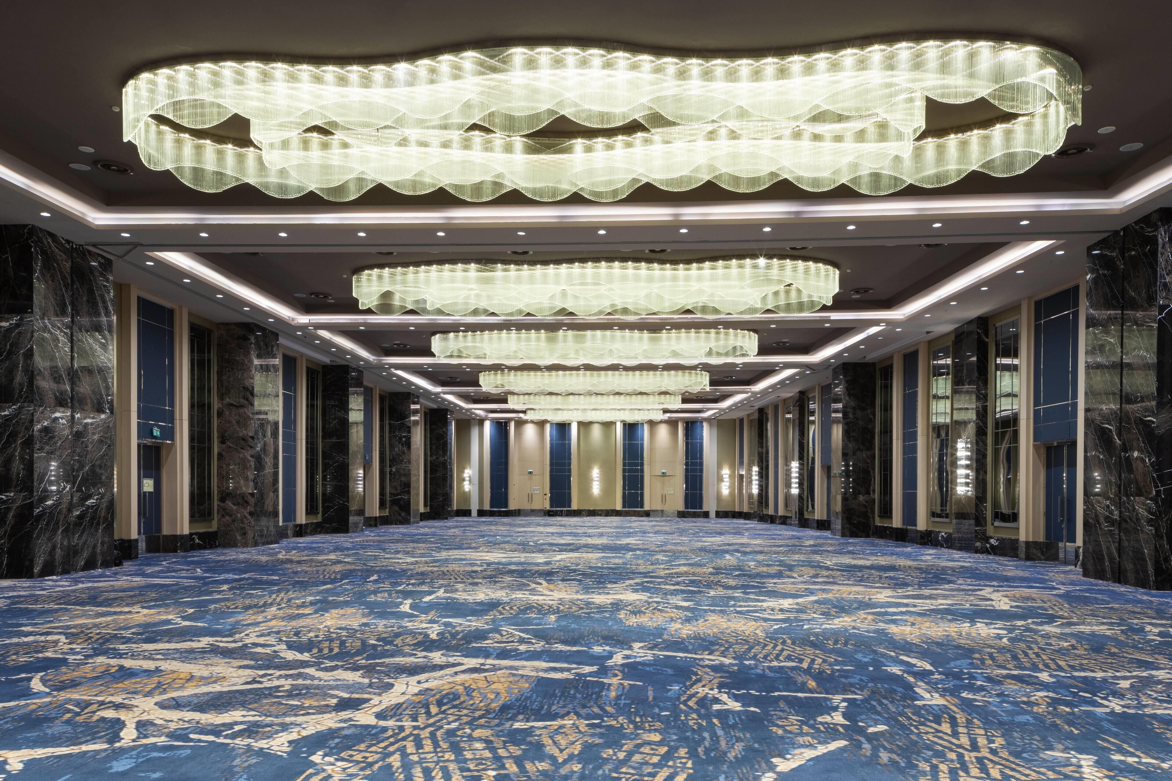 A spacious hotel lobby with a large carpeted area, multiple chandeliers, and marble walls.