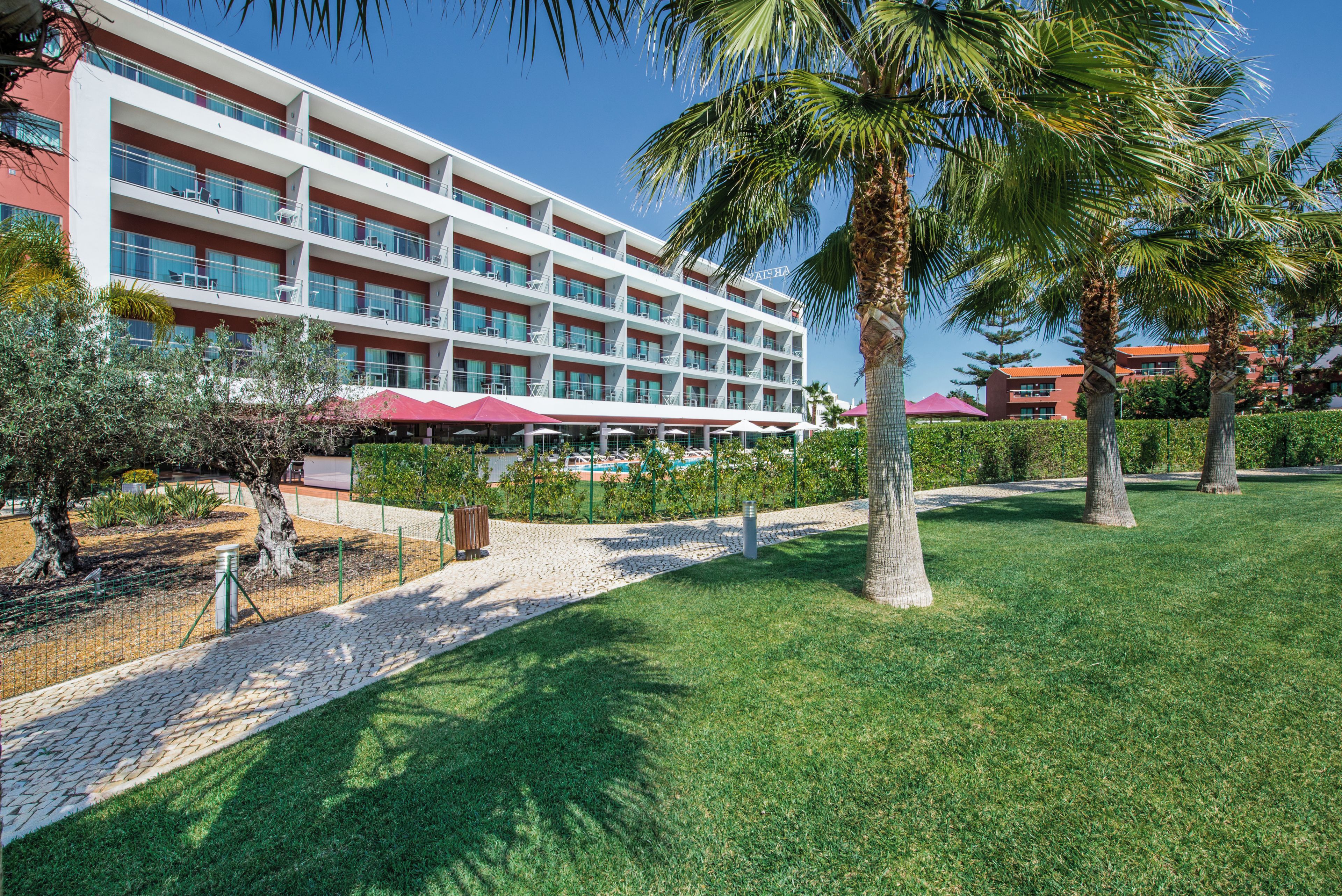 A multi-story hotel with balconies, a swimming pool, and a well-maintained lawn.