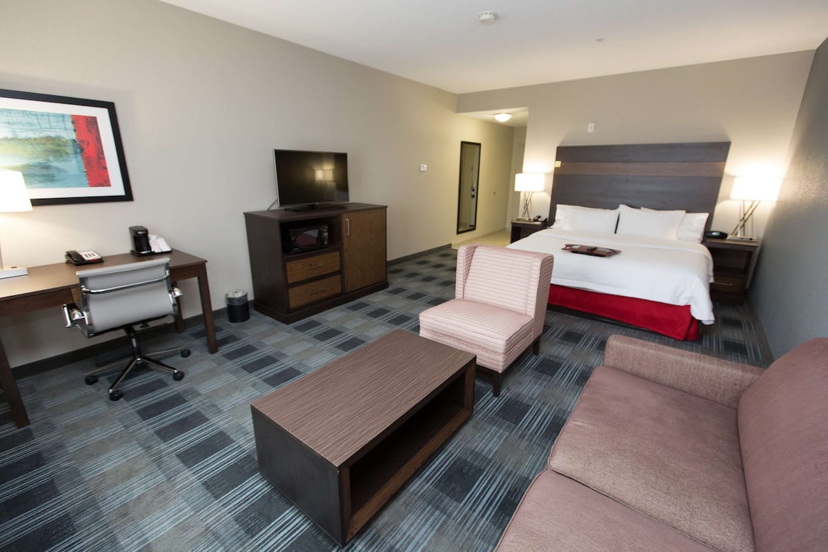 A hotel room with a bed, a desk with a computer, a chair, a coffee maker, and a TV.