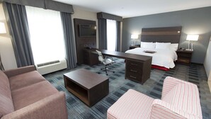 A hotel room with a bed, desk, two chairs, a coffee table, and a TV. - Hampton Inn & Suites Oklahoma City Airport (Oklahoma City)