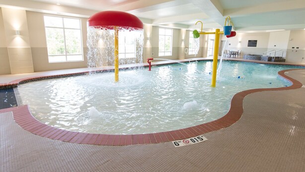 An indoor swimming pool with a water slide, a red umbrella, and a lifeguard stand. - Hampton Inn & Suites Oklahoma City Airport (Oklahoma City)