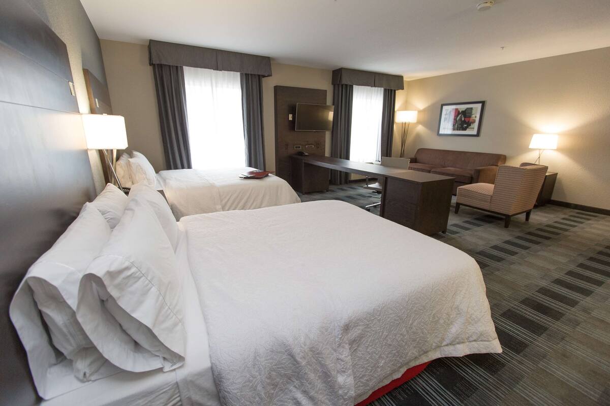 A hotel room with two beds, a desk, a chair, a TV, and a painting on the wall.