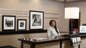 A reception desk with framed historical photos, a welcome sign, a lamp, and a Hilton Honors sign. - Hampton Inn & Suites Oklahoma City Airport (Oklahoma City)