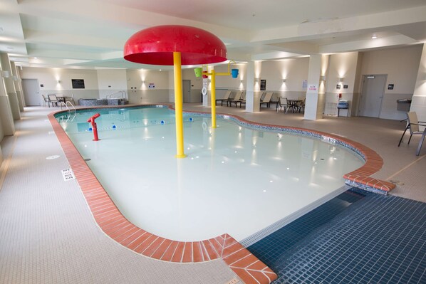 An indoor swimming pool with a red overhead structure, tiled floor, and seating areas. - Hampton Inn & Suites Oklahoma City Airport (Oklahoma City)