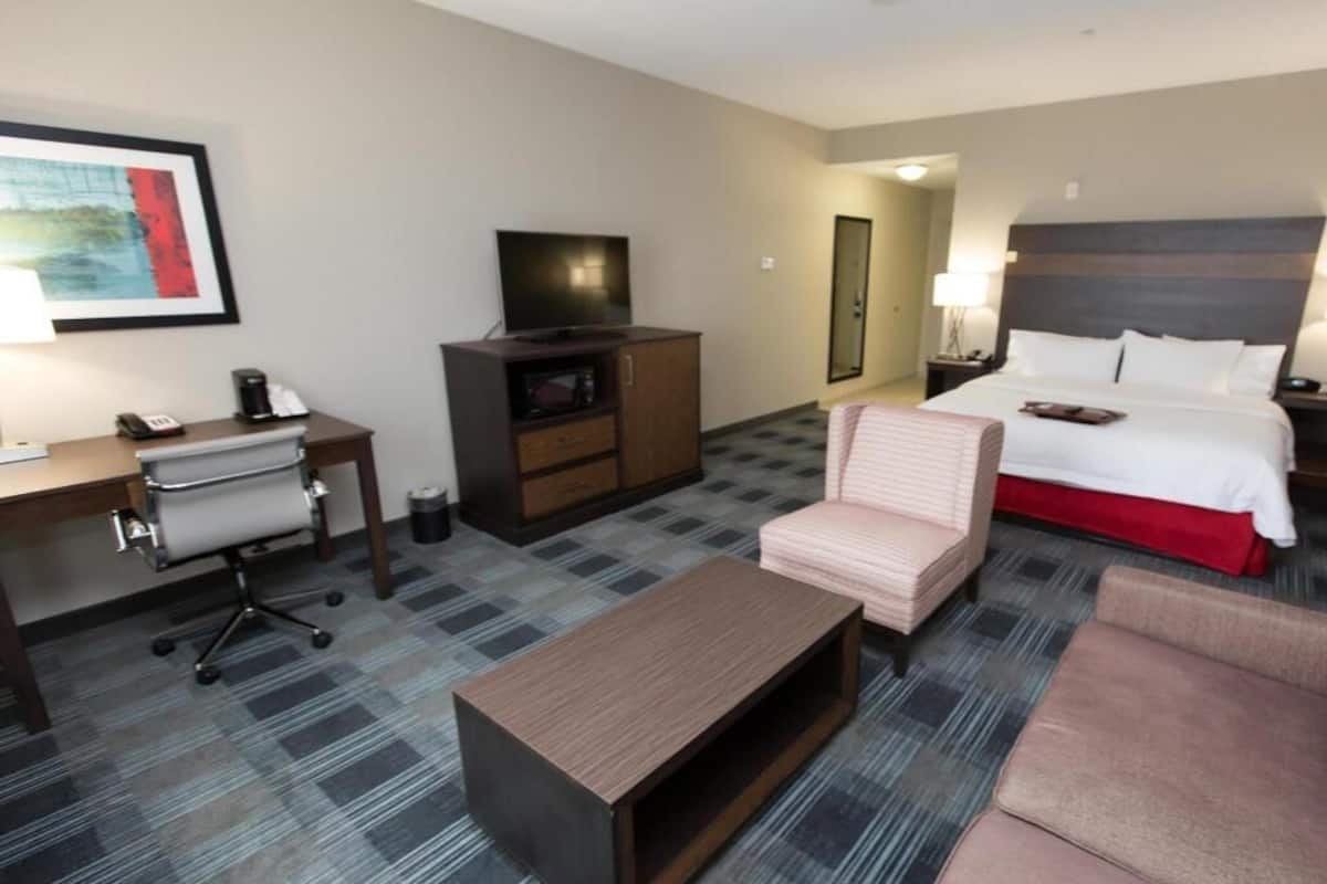A hotel room with a bed, a desk with a chair, a television, a coffee maker, and a lamp.