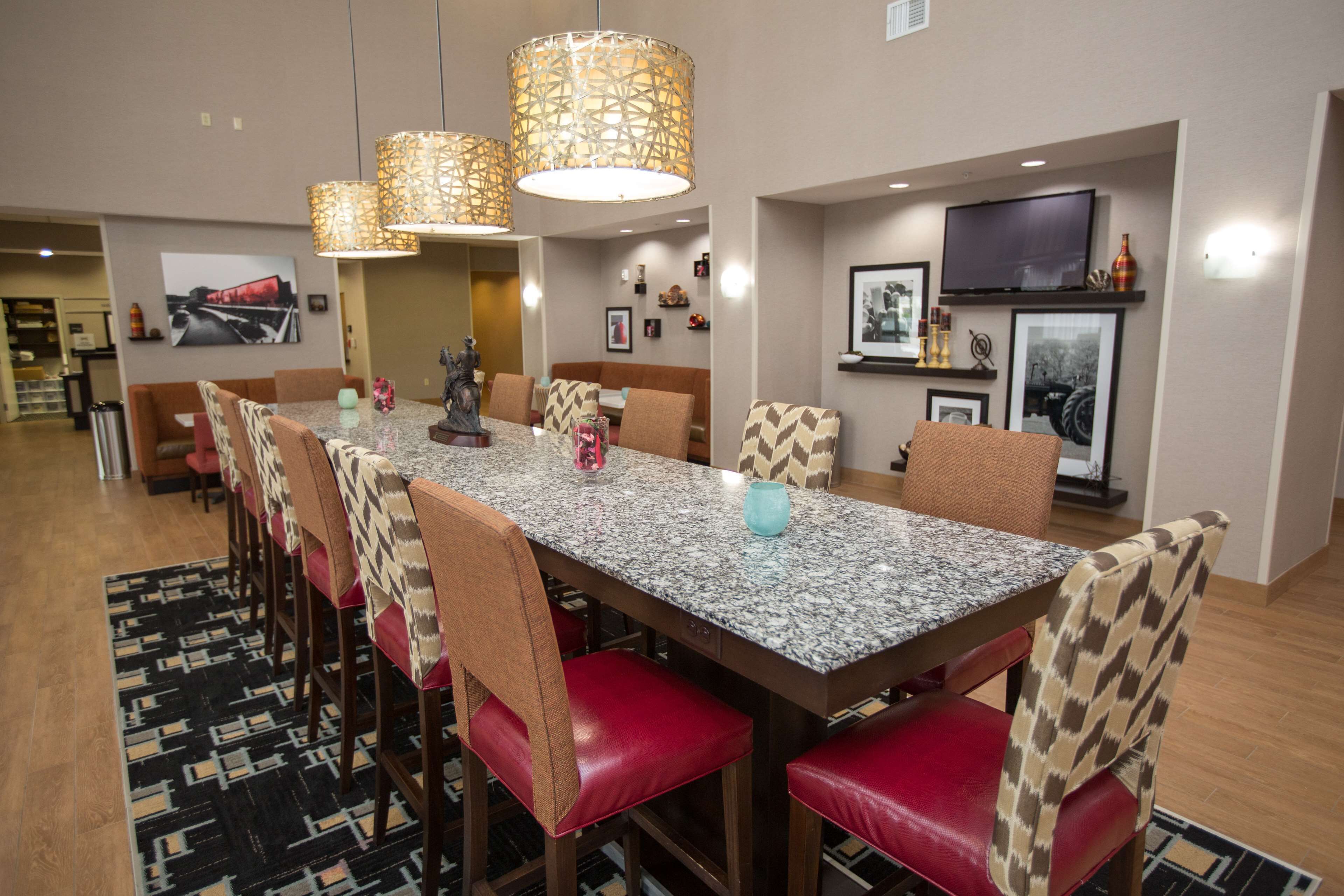 A dining area with a long table, red cushioned chairs, patterned lamps, and framed pictures on the walls.