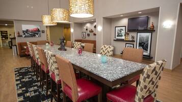 A dining area with a long table, red cushioned chairs, patterned lamps, and framed pictures on the walls.