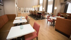 A modern dining area with booths and tables, featuring a central dining table with chairs, pendant lighting, and a patterned rug. - Hampton Inn & Suites Oklahoma City Airport (Oklahoma City)