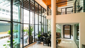 A spacious lobby with a modern design, featuring a large seating area with a sofa and chairs, a staircase, and large windows offering views of the outside. - Amber Boutique Silom Hotel (Bangkok)