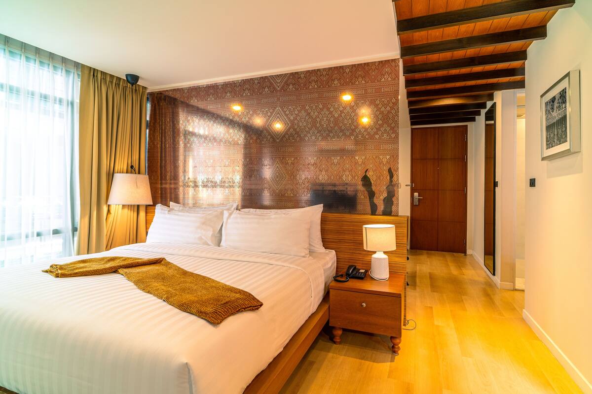 A hotel room with a large bed, a bedside table with a lamp, a telephone, and a wooden headboard.