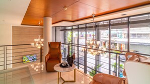A spacious lobby with a high ceiling, large windows offering a view of the street, a comfortable seating area with leather chairs, and a small table with a decorative item. - Amber Boutique Silom Hotel (Bangkok)
