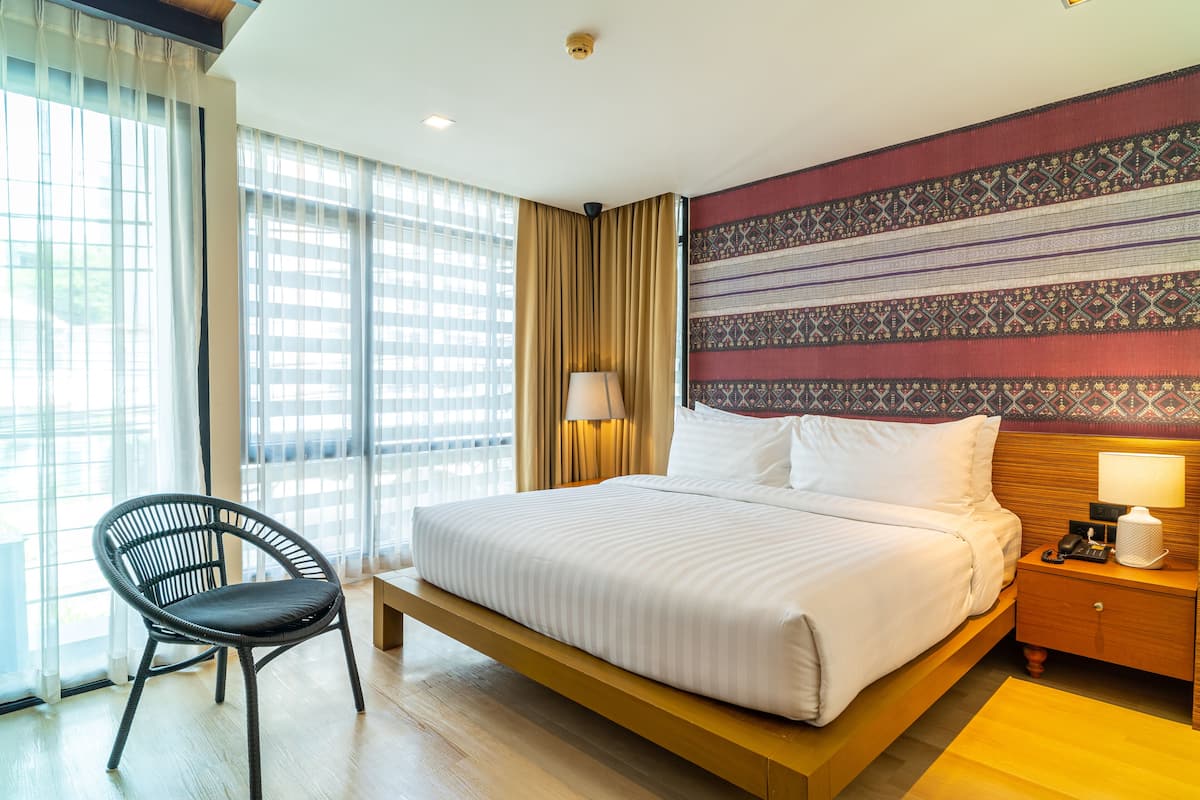 A hotel room with a bed, a chair, a nightstand, and a patterned wall.