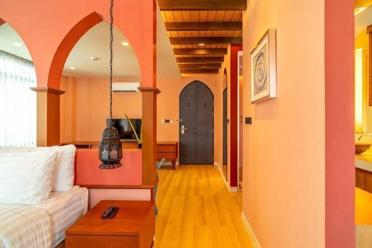 A hotel room with a bed, a wooden coffee table, a hanging lantern, and a door leading to another room.