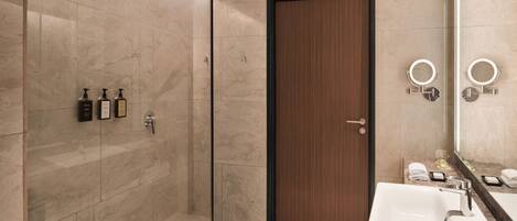 A modern bathroom with a glass shower enclosure, a wooden door, a white sink with a mirror, and toiletries on the wall.