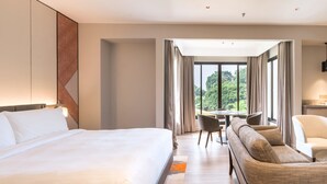 A hotel room with a large bed, a sofa, a dining table, and a view of the outdoors. - Palm Garden Hotel, Putrajaya, a Tribute Portfolio Hotel (Serdang)