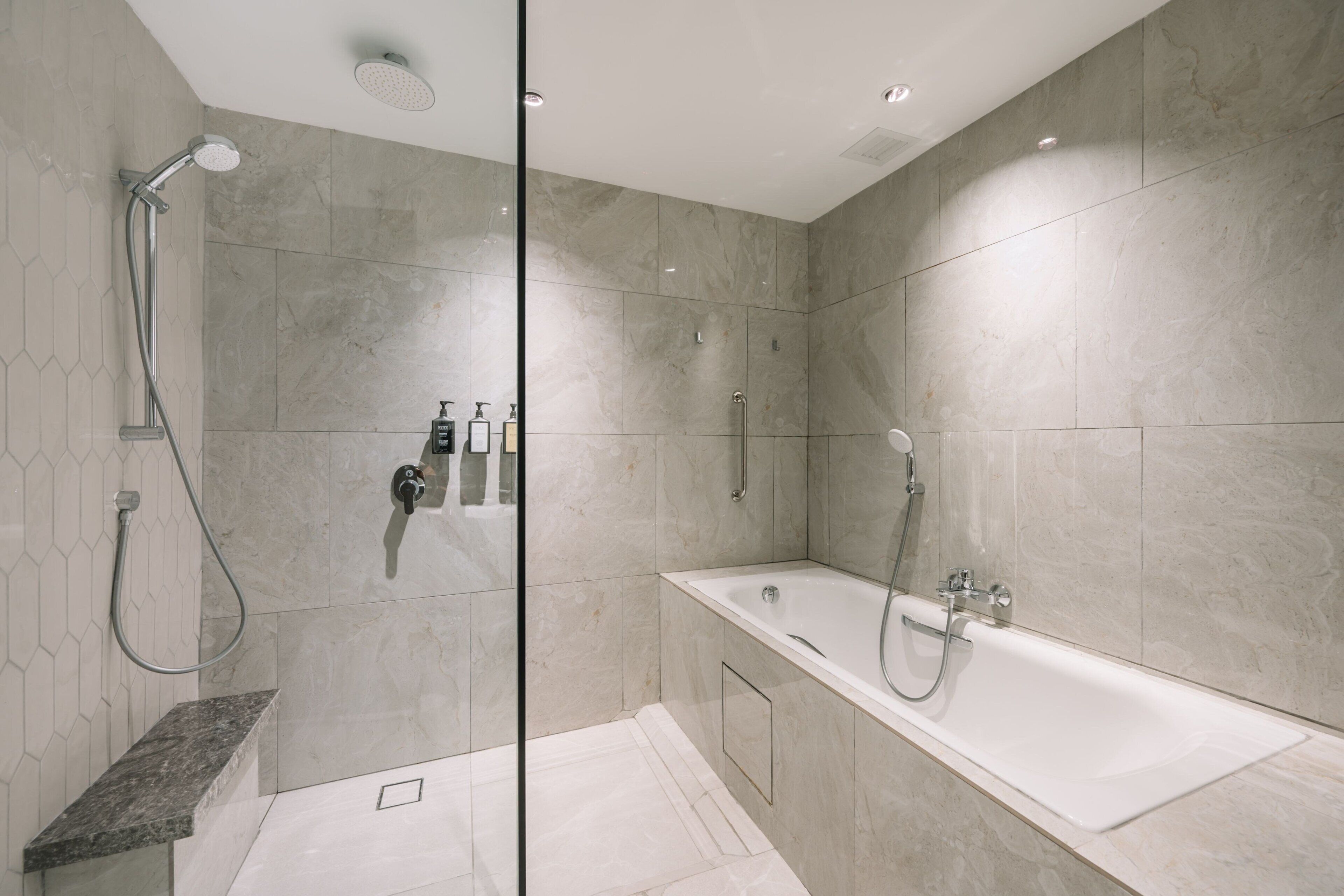 A modern bathroom with a glass-enclosed shower, a freestanding bathtub, and a marble-tiled floor.