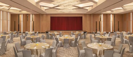 A banquet hall with round tables, grey chairs, and a large red stage.