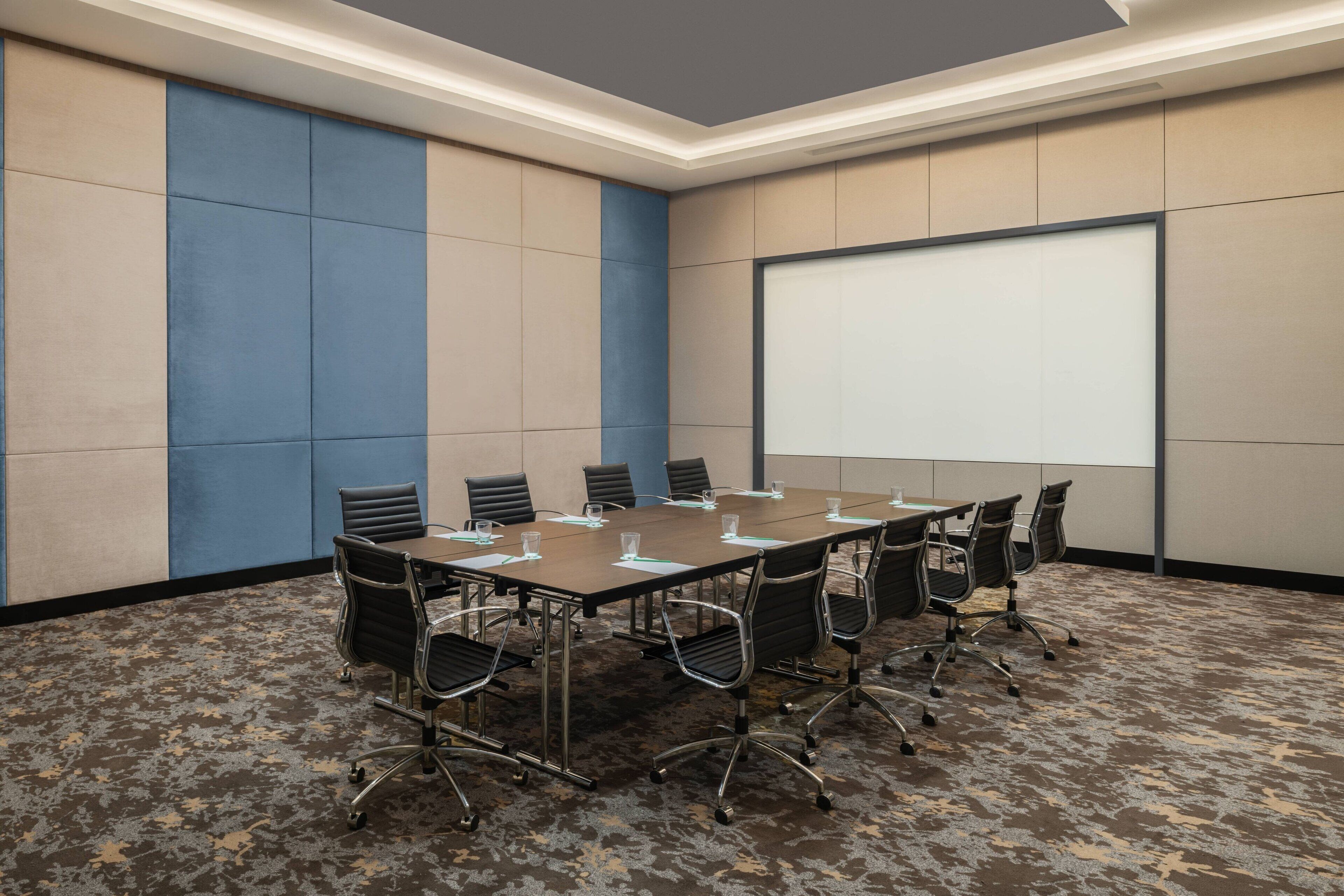 Un salón de conferencias con una amplia mesa, sillas y una pantalla de proyector.