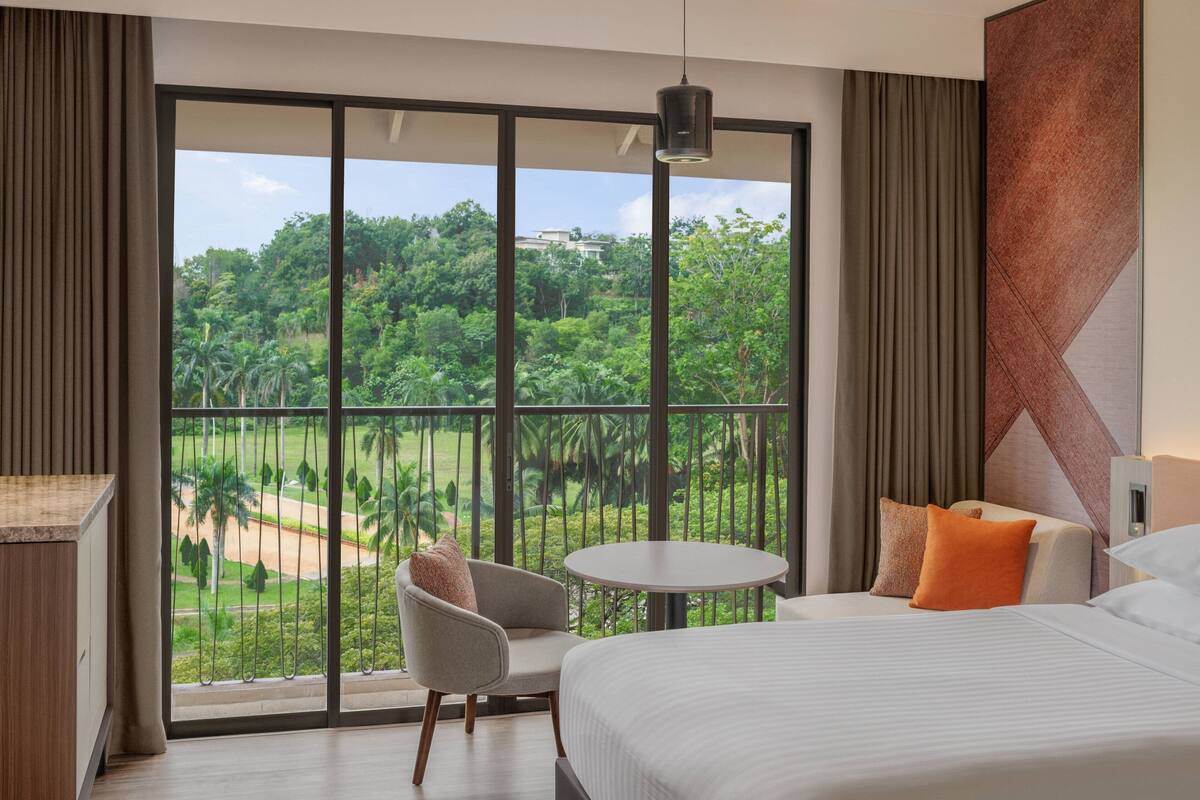 A hotel room with a large balcony, a bed, a round table, and a chair.