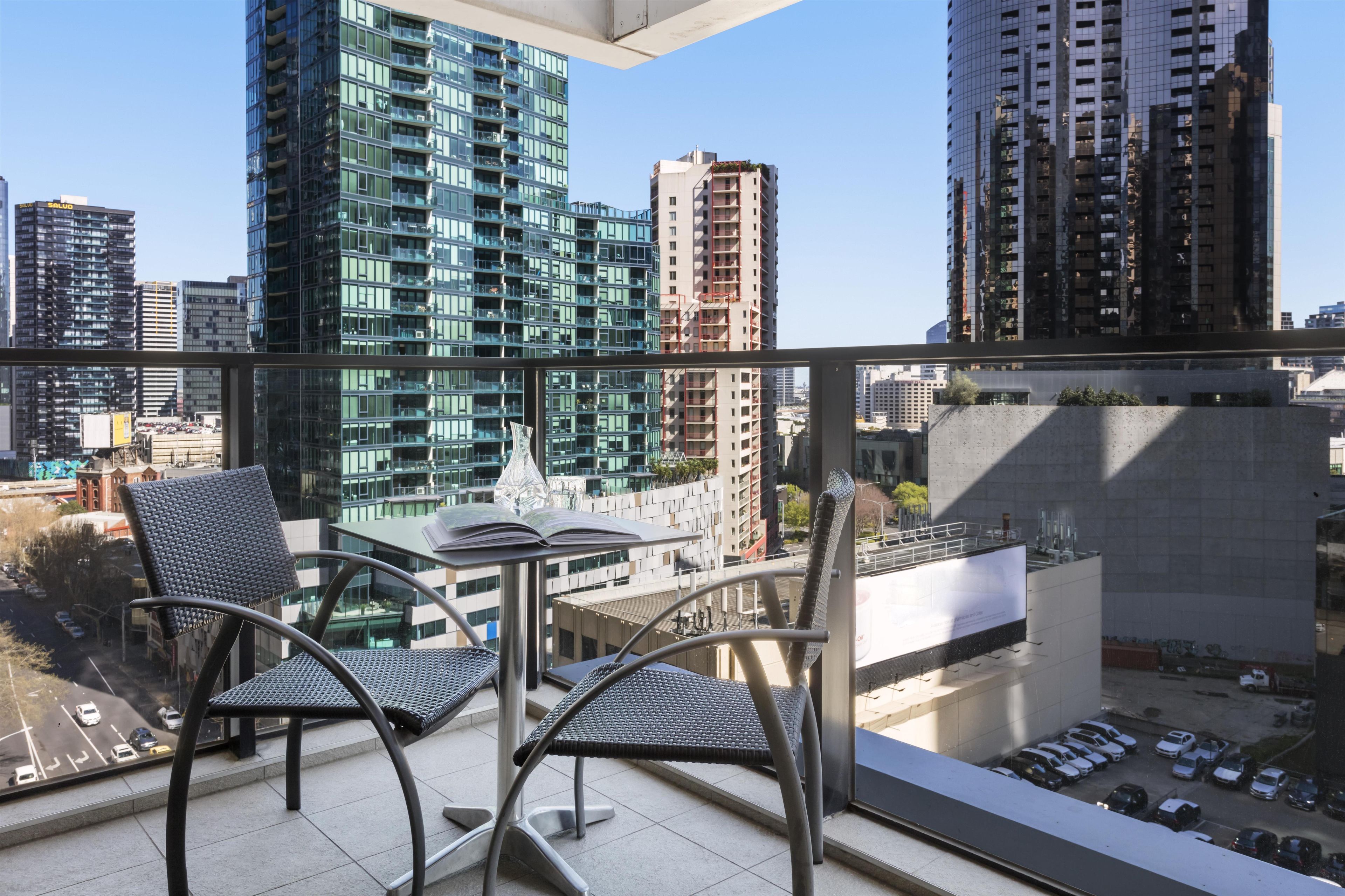 Un balcón con dos sillas y una mesa, con vista a un paisaje urbano de edificios modernos.