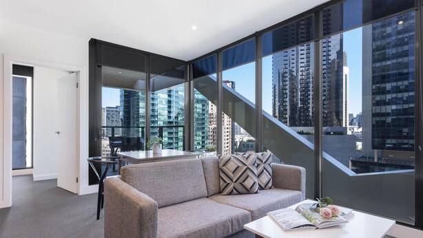 A modern living room with a sofa, a coffee table, and a view of high-rise buildings through large windows. - WRAP on Southbank (Southbank)