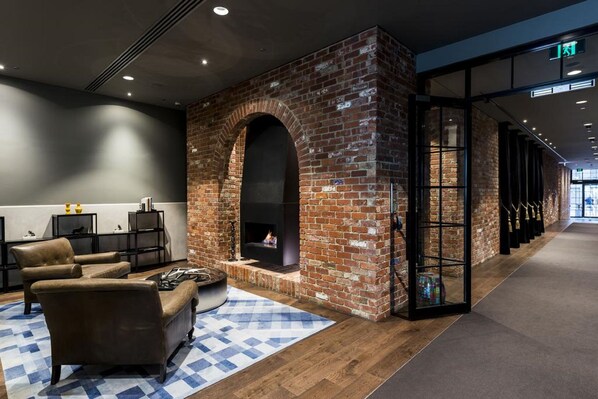 A modern lounge area with a brick fireplace, leather sofas, and a checkered rug. - WRAP on Southbank (Southbank)